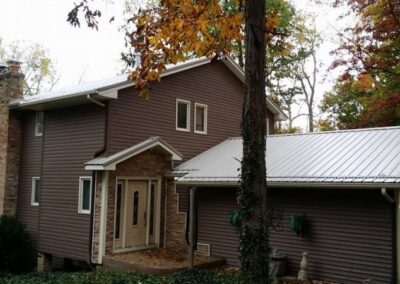 a brown house with a metal roof in the woods